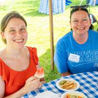 Tricia Augdahl '02 and woman smile in between bites of food